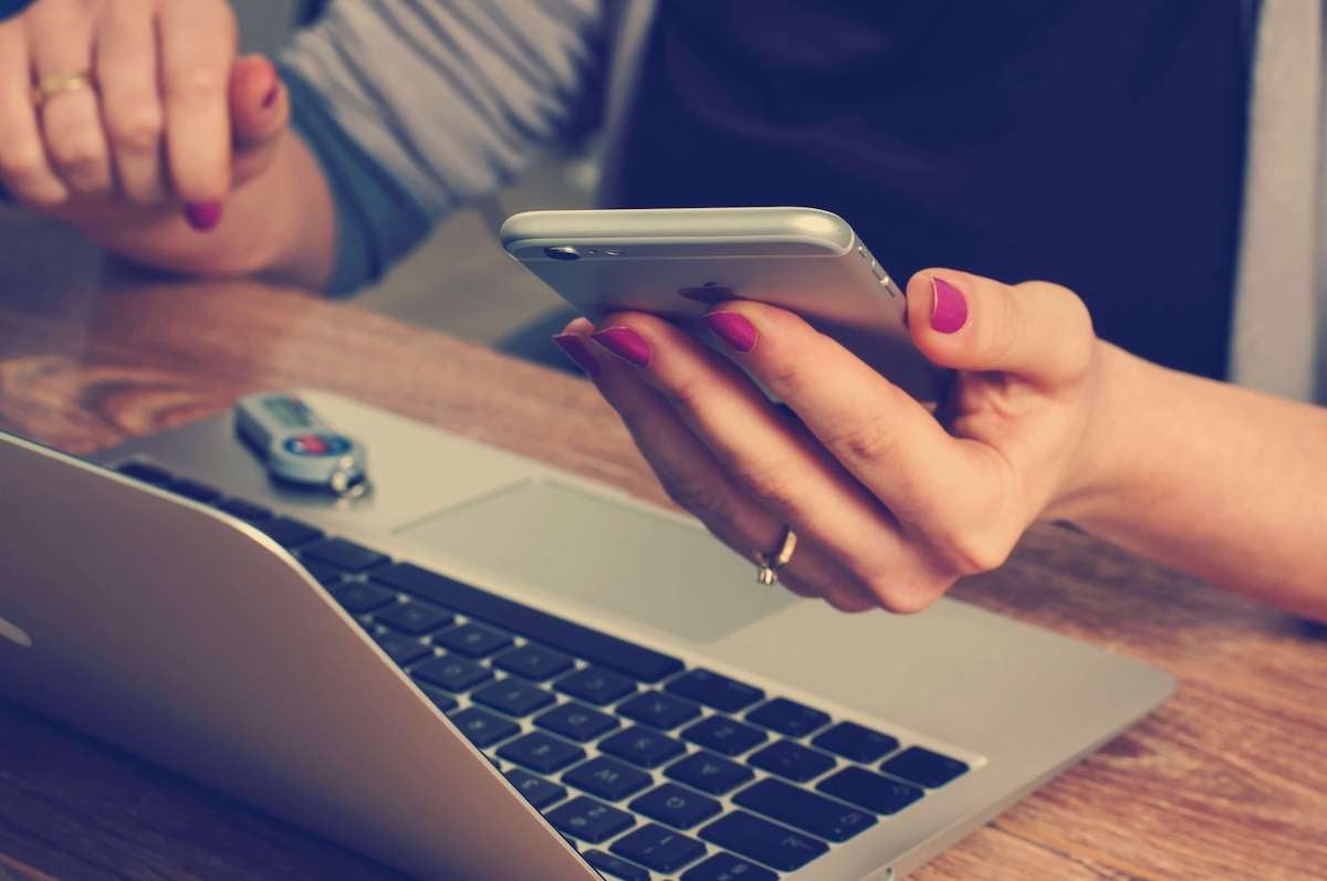 Woman holding a phone in front of the laptop.